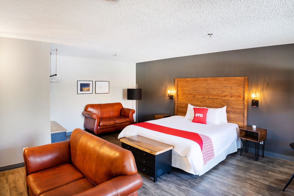 A hotel room with a large bed, two brown leather chairs, a wooden headboard, and a small wooden table.