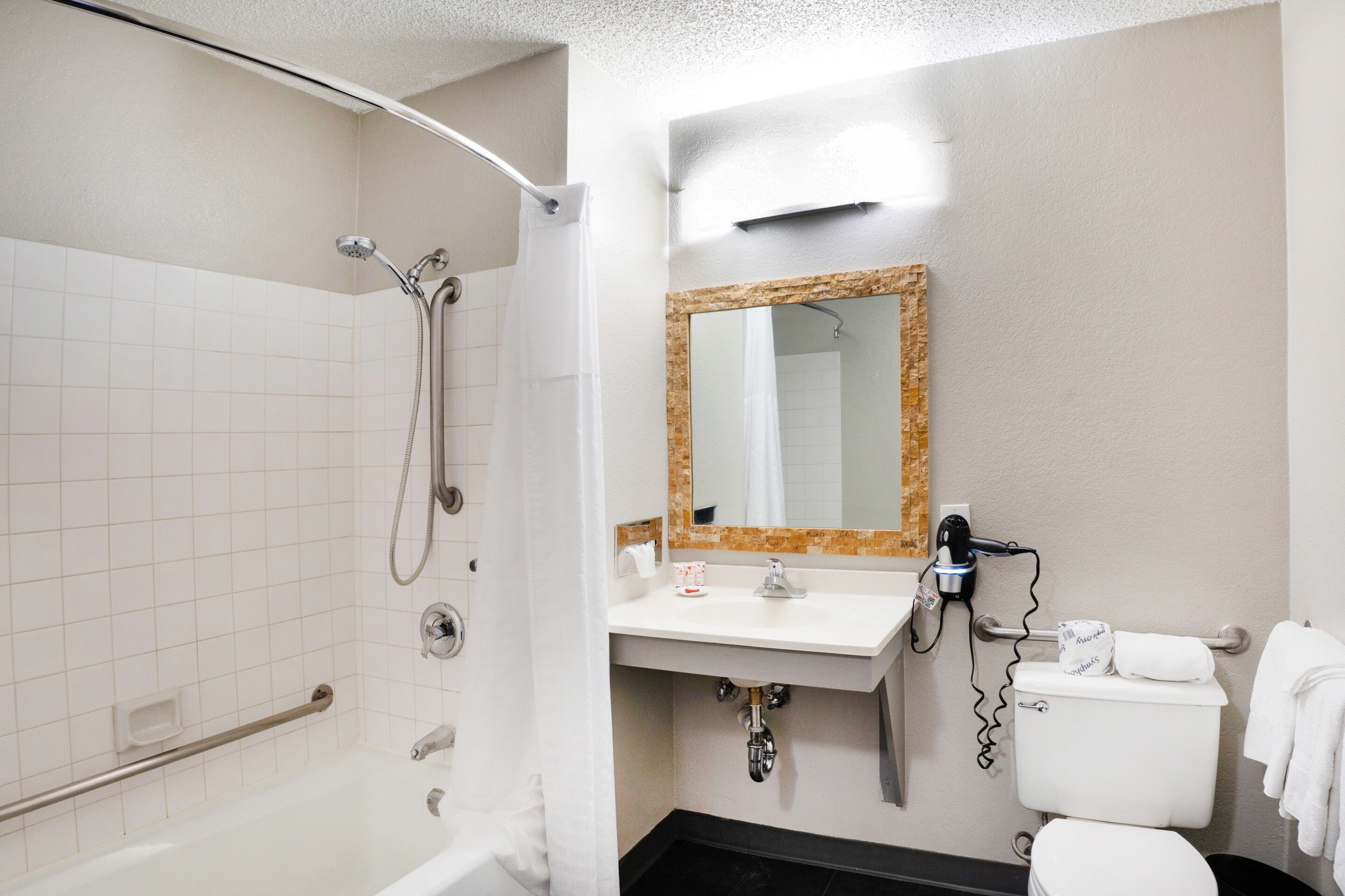 A bathroom with a shower, toilet, sink, and a mirror with a wooden frame.
