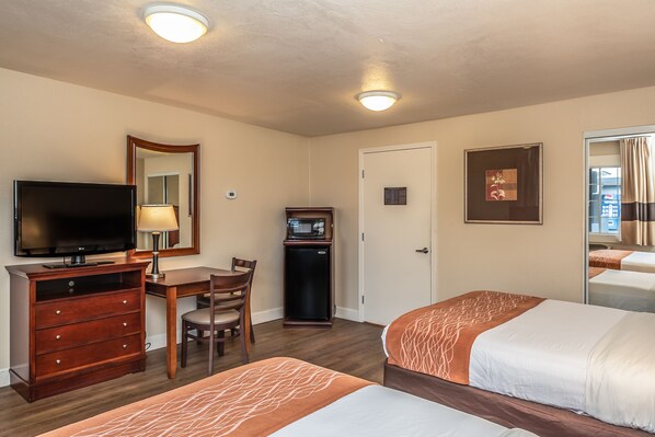A hotel room with two beds, a desk with a chair, a television, a small refrigerator, and a mirror.