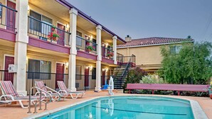 Un hotel con piscina, sillones de descanso y balcones con plantas en macetas.
