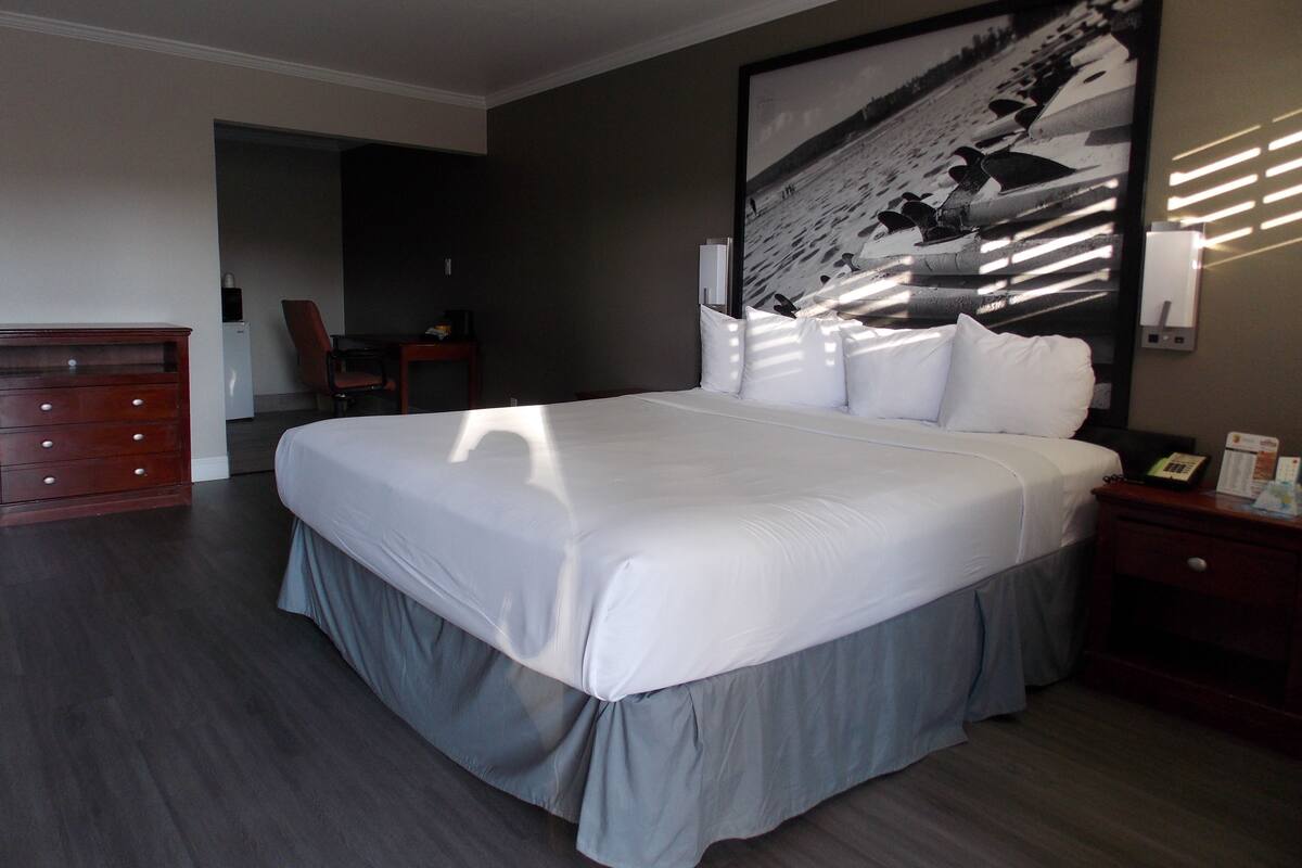 Habitación de hotel con una cama grande, un escritorio, una silla, un aparador y un cuadro grande en la pared.