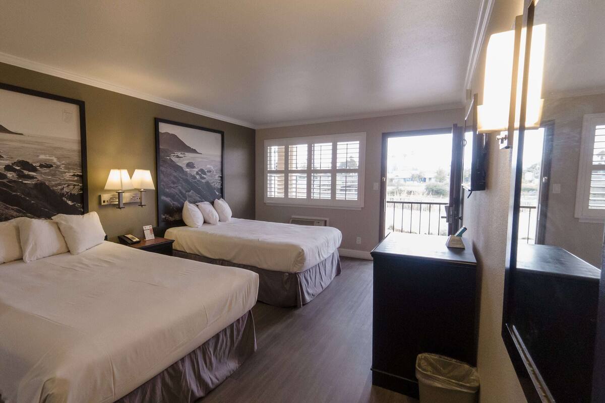 Habitación de hotel con dos camas, un escritorio, una silla, un cubo de basura y un ventanal con vistas.