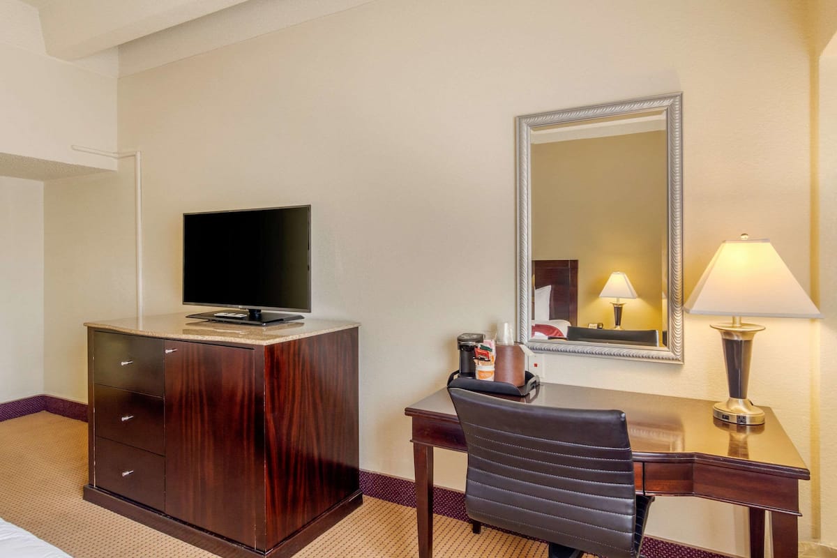 Une chambre d’hôtel avec un bureau en bois, un téléviseur posé dessus, un miroir et une lampe.