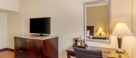 A hotel room with a wooden desk, a television on top, a mirror, and a lamp.