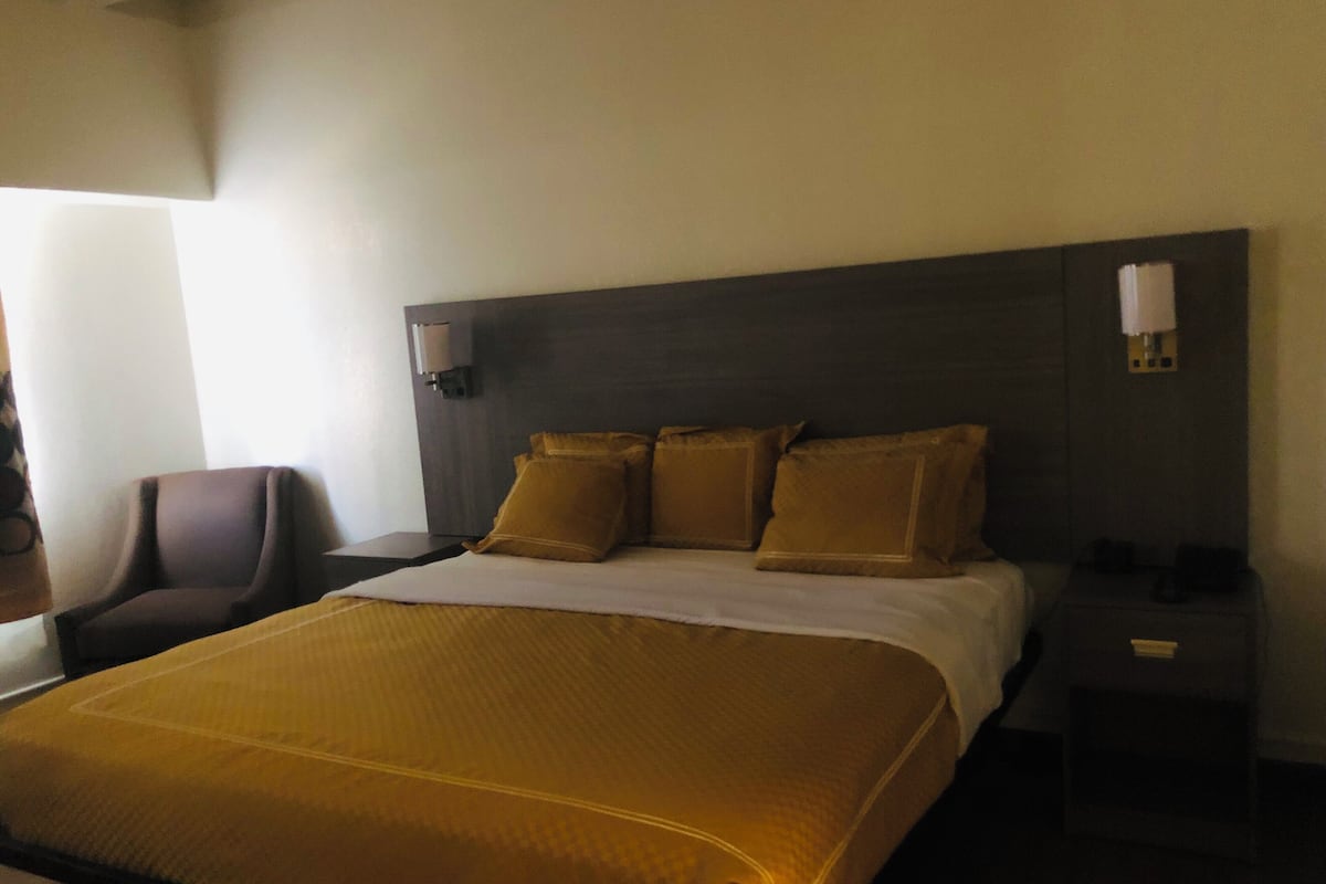 Une chambre d’hôtel avec un grand lit, une chaise, une table de chevet et une lampe fixée au mur.
