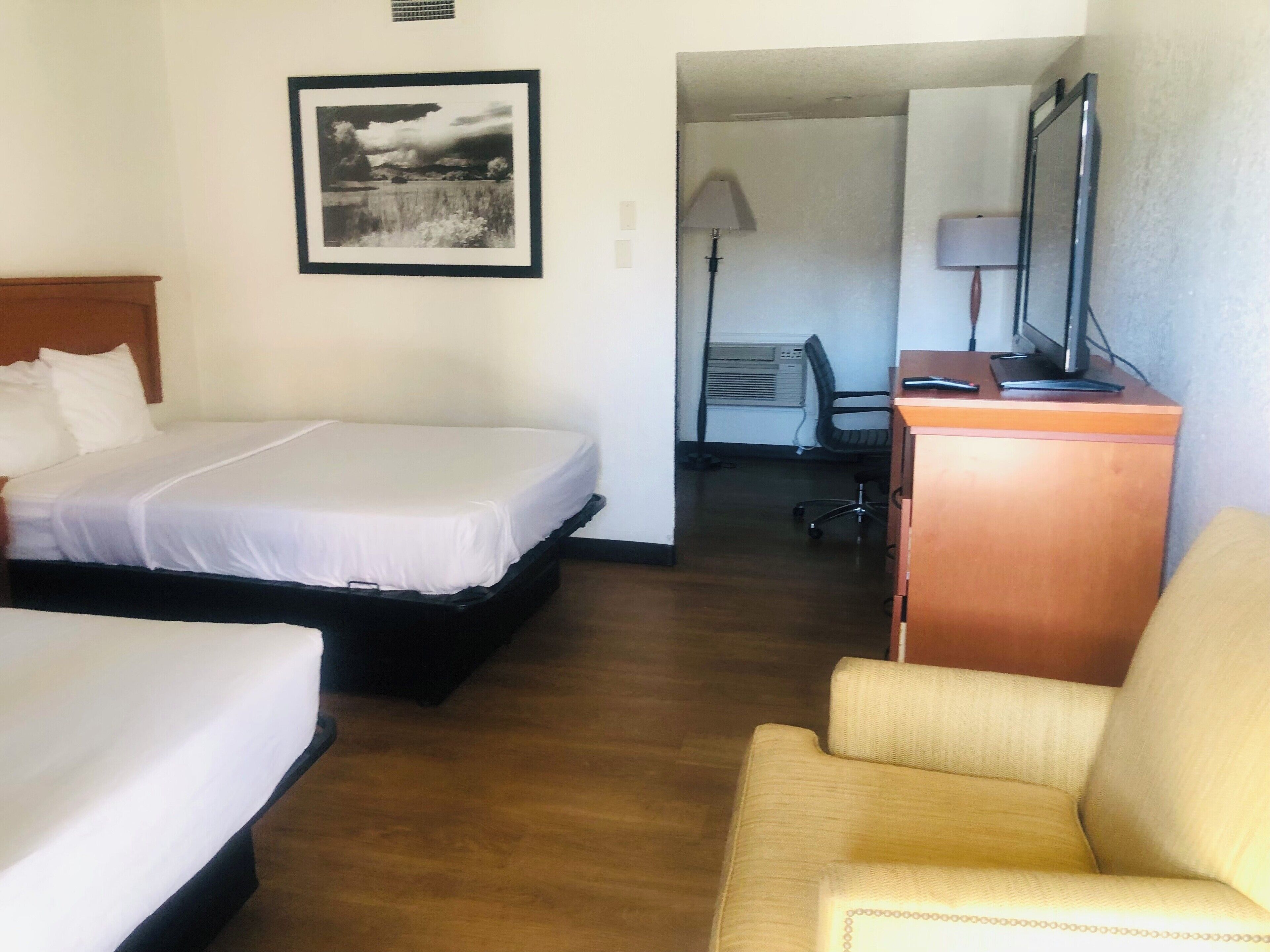 A hotel room with two beds, a desk with a computer, a chair, and a framed picture on the wall.