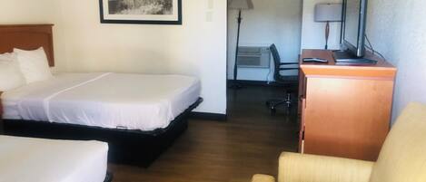A hotel room with two beds, a desk with a computer, a chair, and a framed picture on the wall.