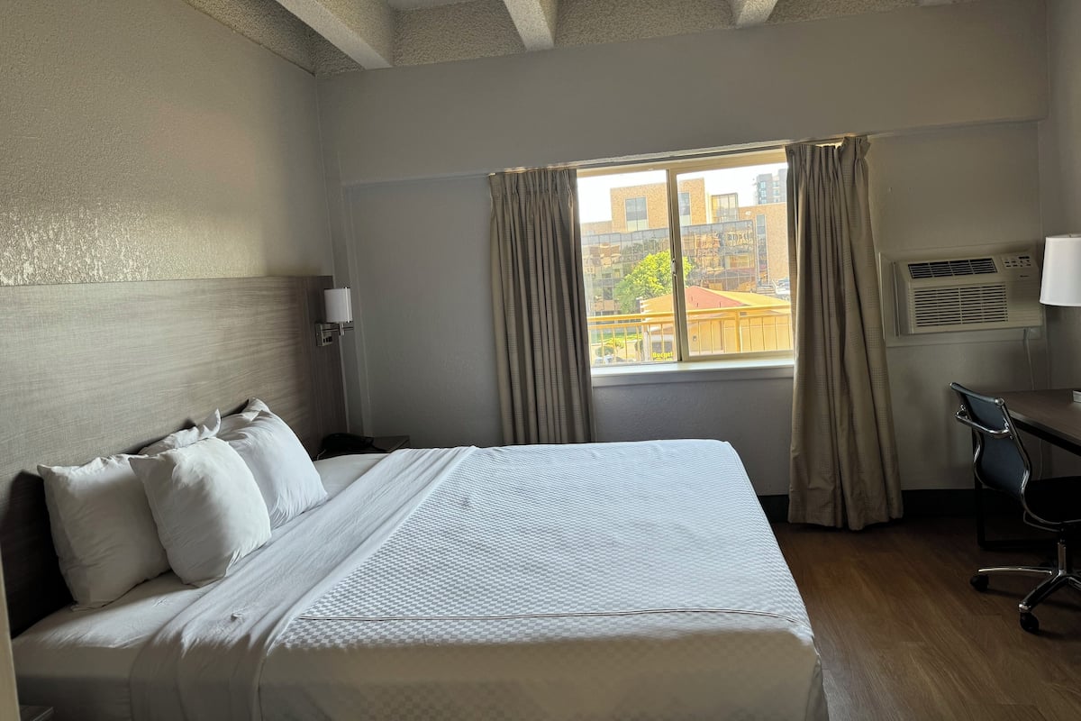 Une chambre d’hôtel avec un grand lit, un bureau, une chaise, une fenêtre avec des rideaux et un appareil de climatisation.