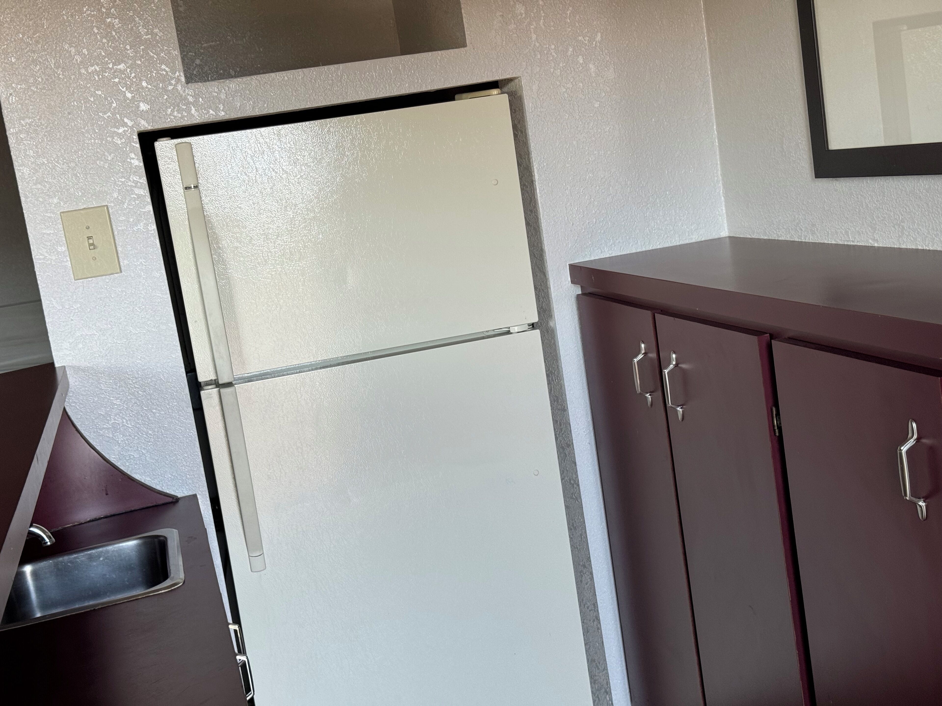 A kitchen with a white refrigerator, a stainless steel sink, and dark wooden cabinets.
