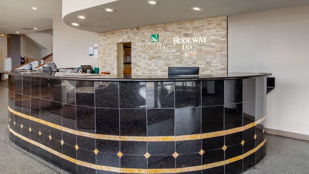 A reception area with a black marble counter, a stone wall with the logo and name of Quality Inn, and a staircase in the background. - Inn at the Highland Denver Downtown (Denver)