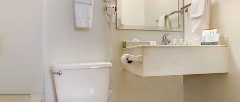 A bathroom with a toilet, a sink with toiletries, a towel rack, and a mirror.