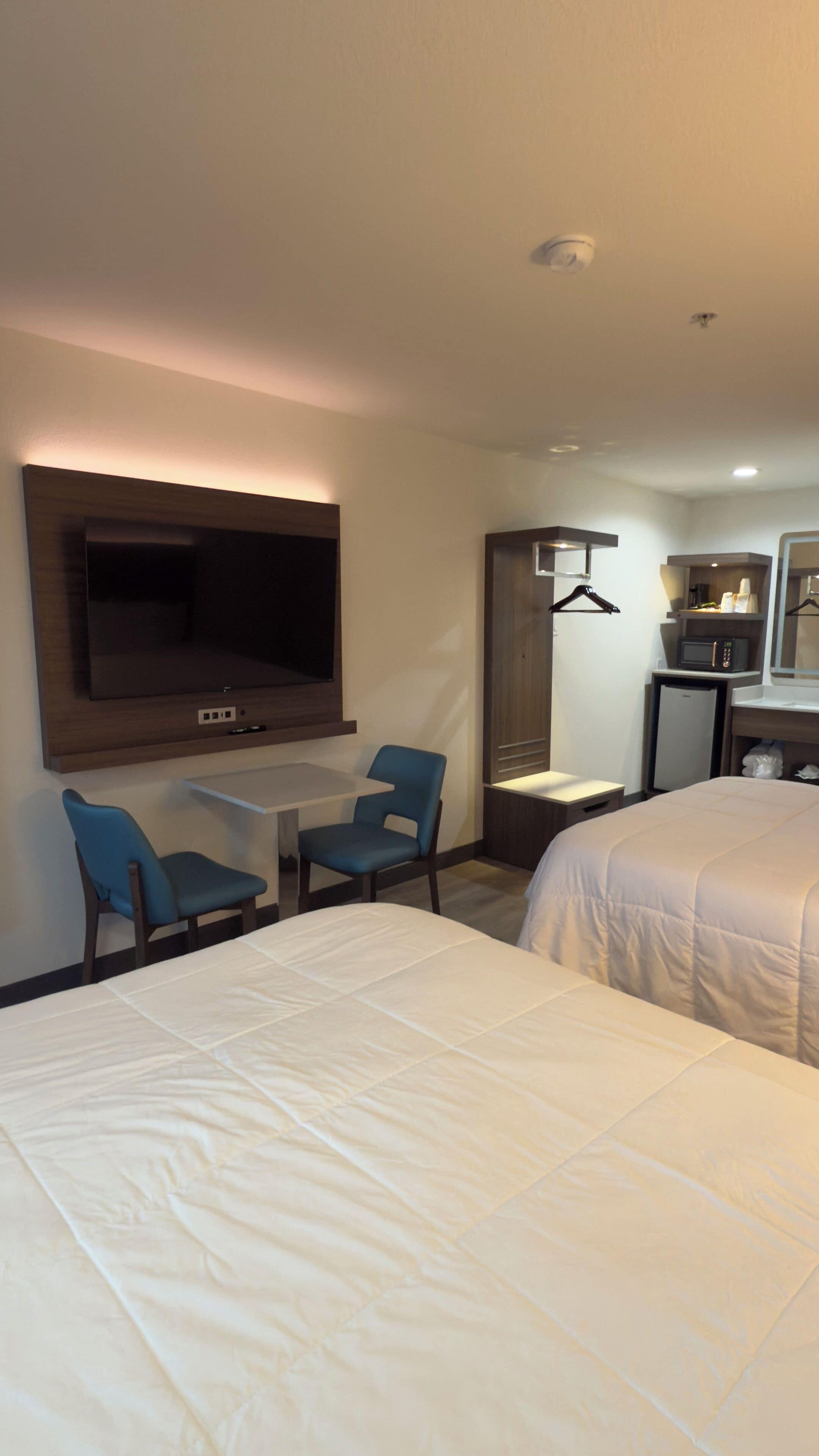 A hotel room with a bed, a TV mounted on the wall, a small table, two chairs, a microwave, and a mini fridge.
