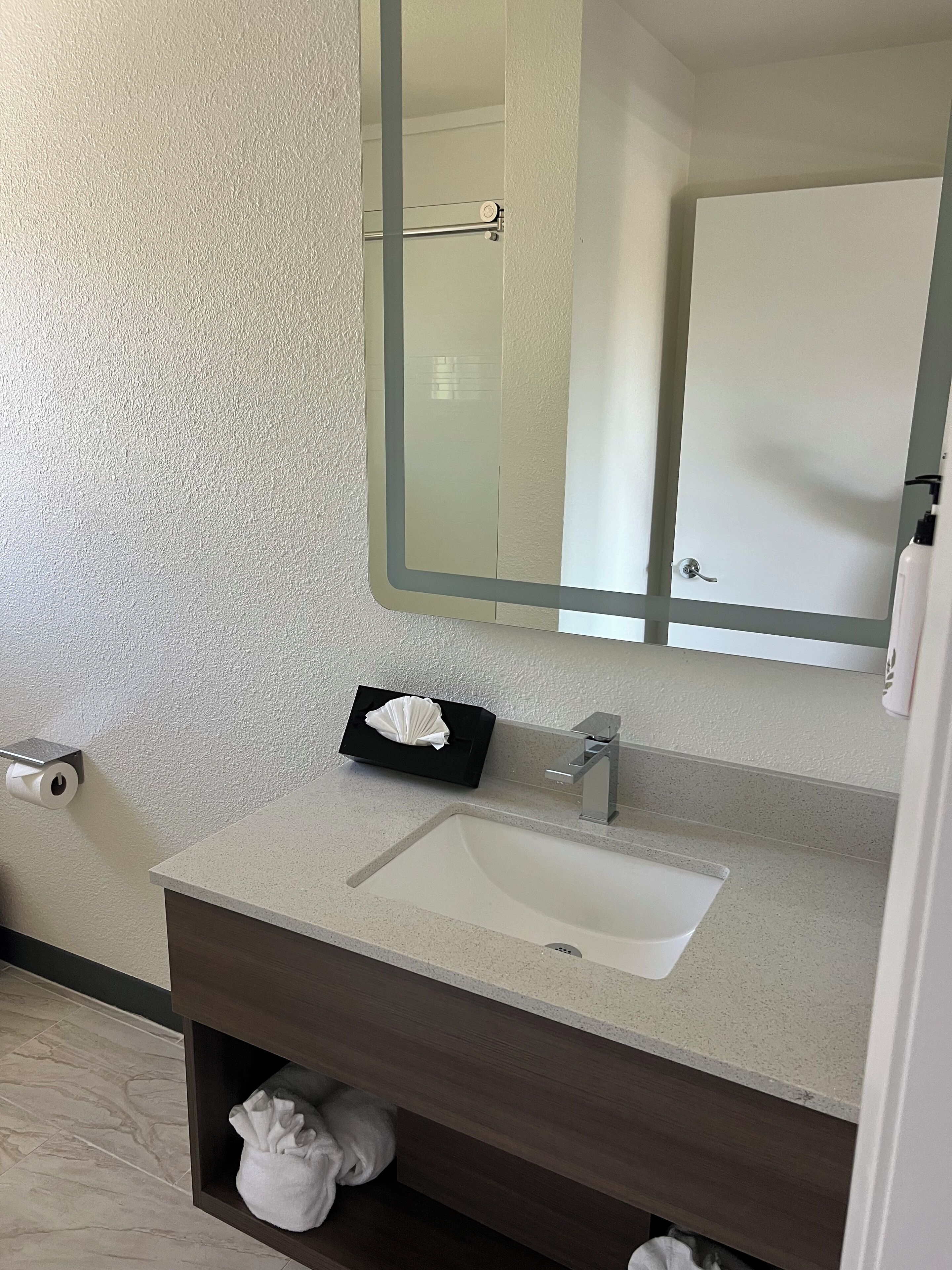 Une salle de bain avec un lavabo blanc, un miroir, un porte-serviettes et un support à papier toilette.