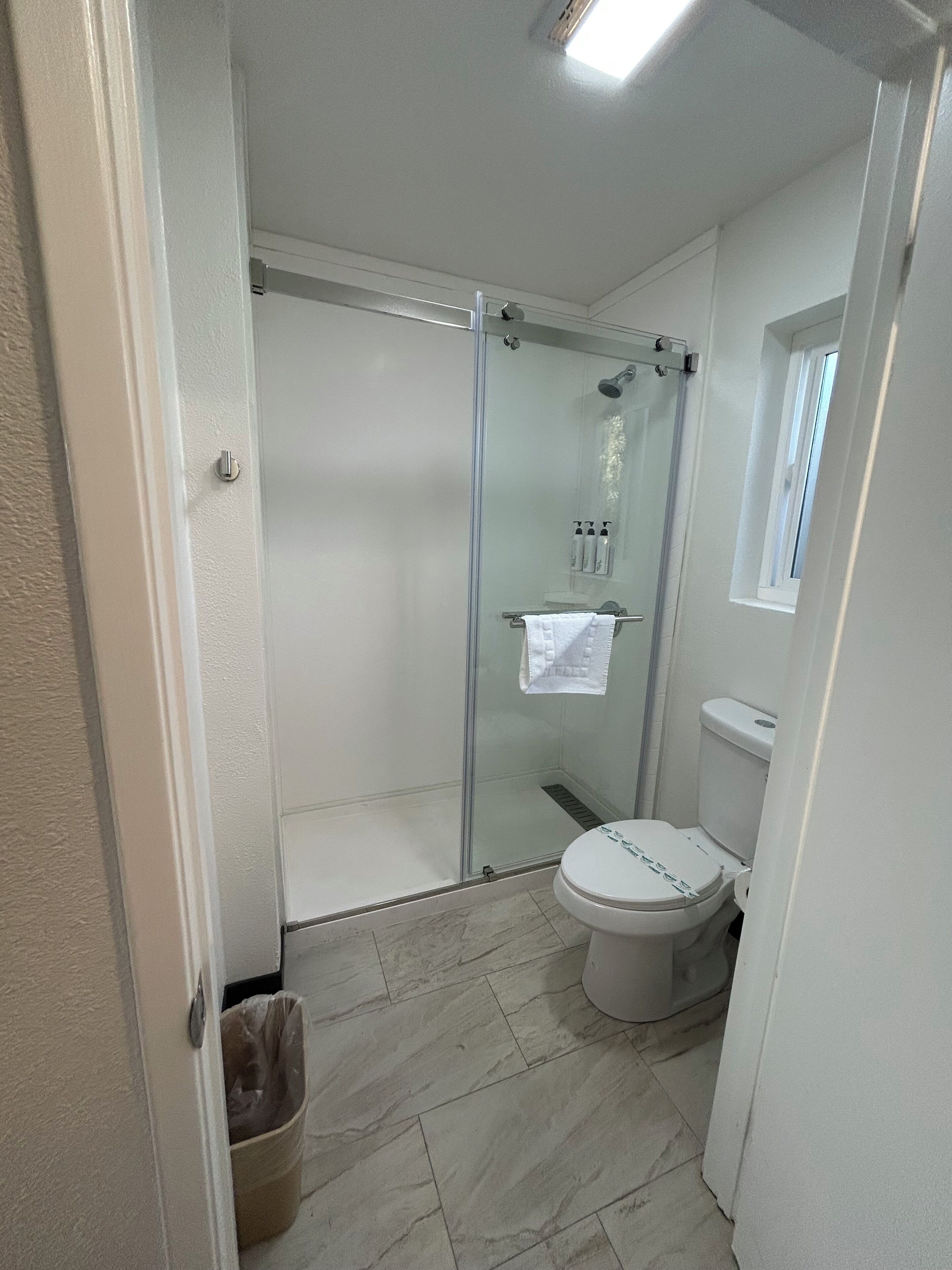 A bathroom with a glass-enclosed shower, a toilet, and a small window.