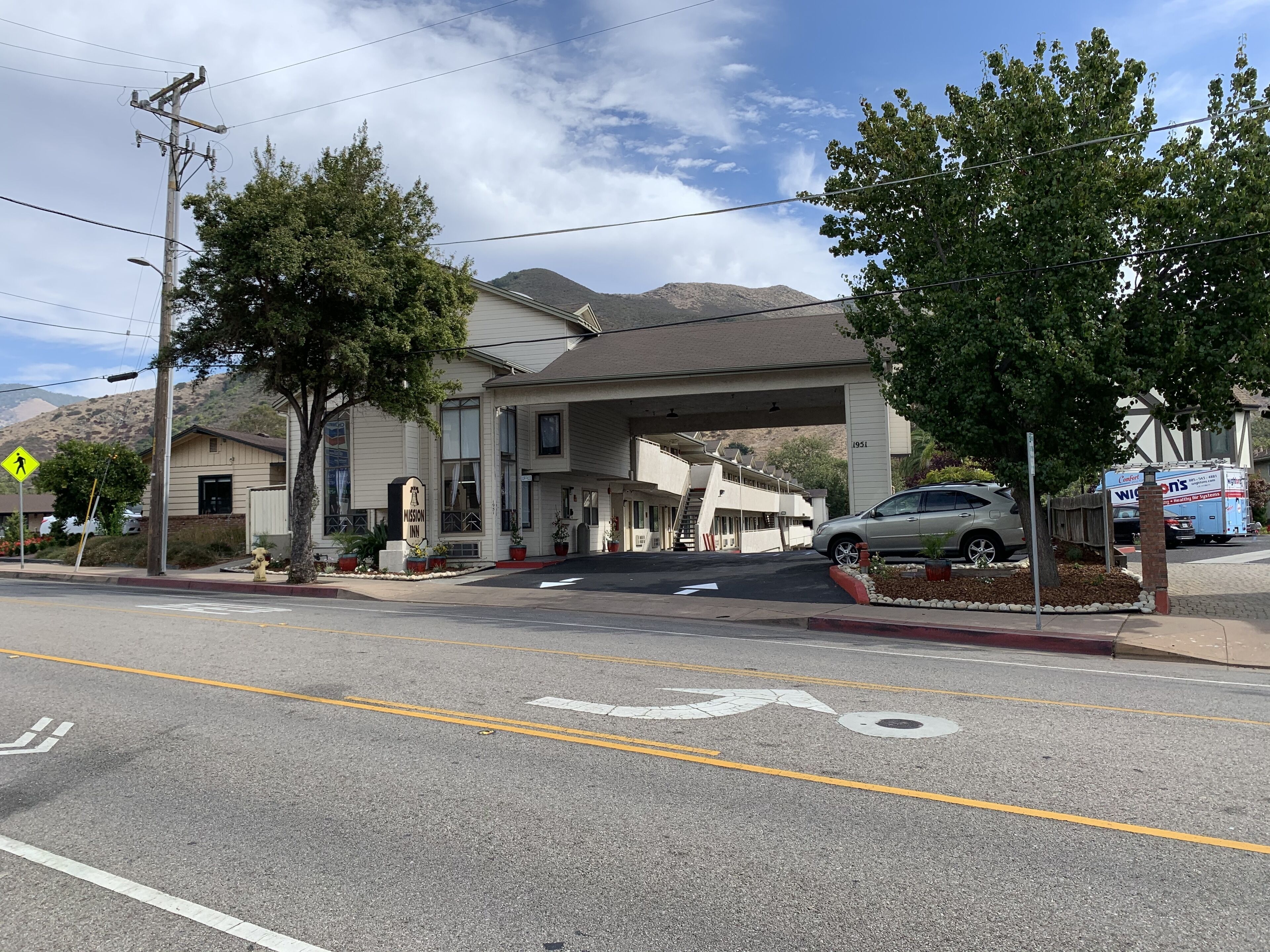 A Mission Inn with a two-story structure, a covered entrance, and a parking area with a car.