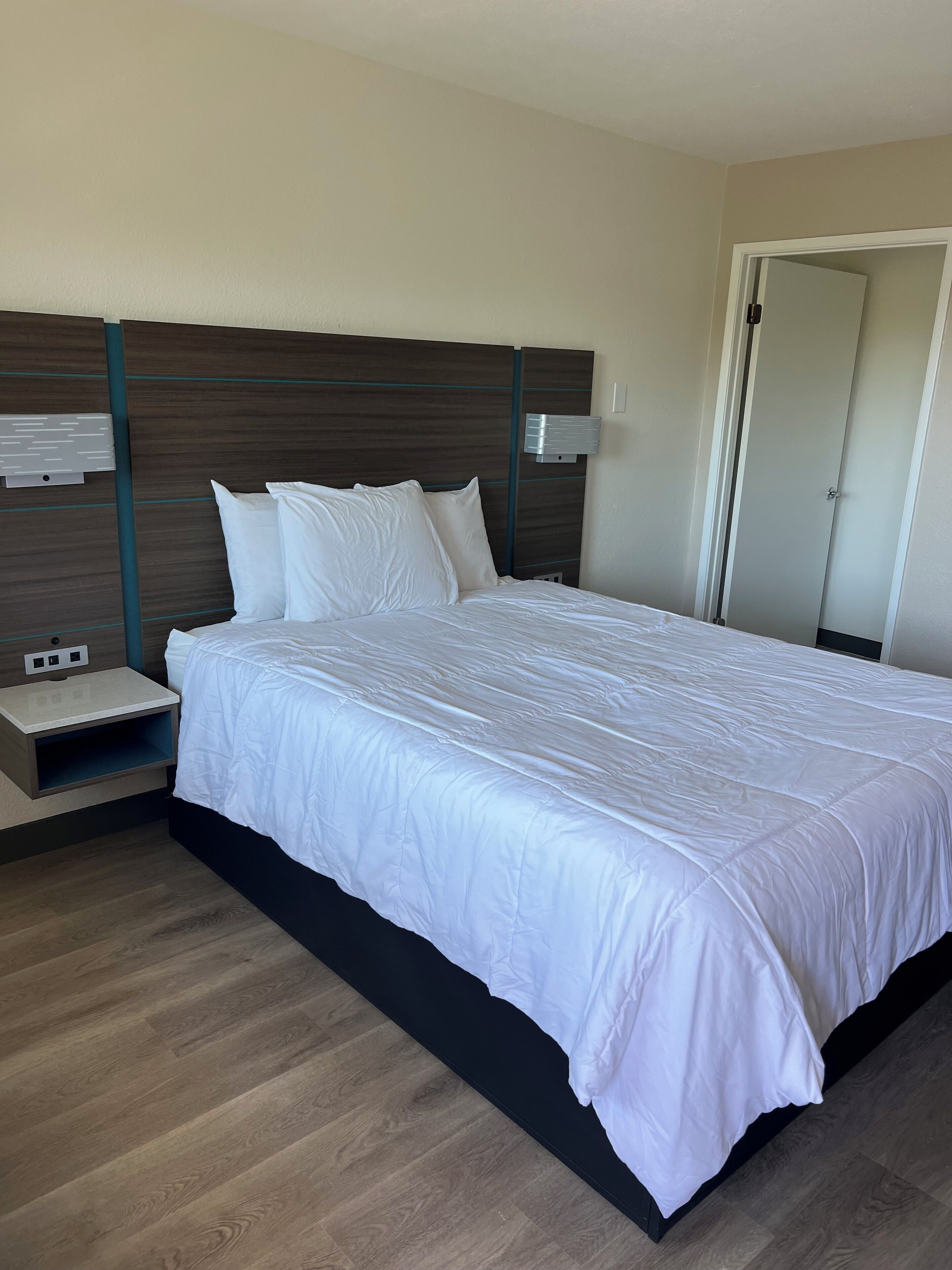 Habitació d'hotel amb un llit gran, una tauleta de nit, una làmpada penjada a la paret i una porta.