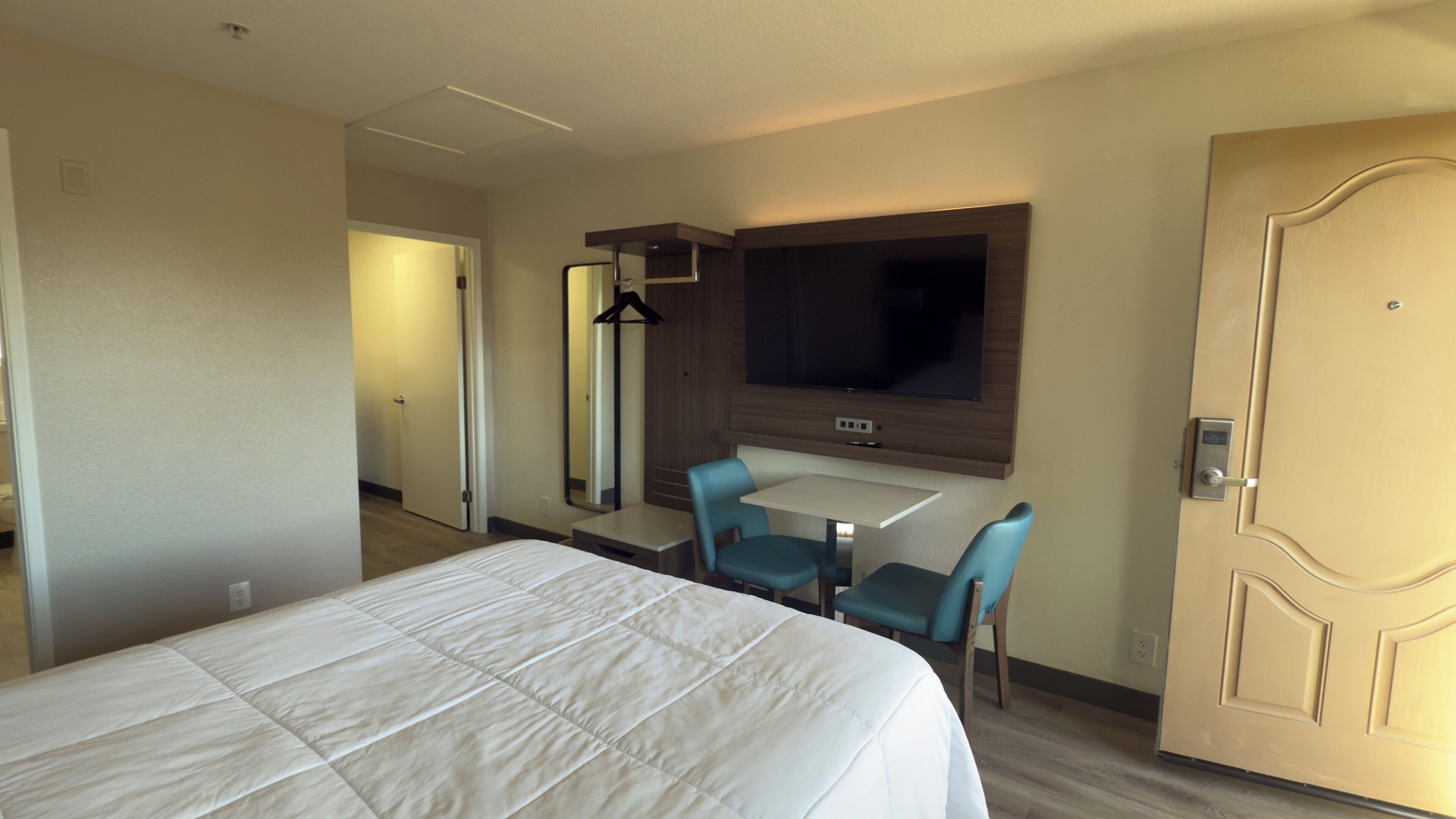 Una habitación de hotel con cama, escritorio, dos sillas, televisor y puerta.