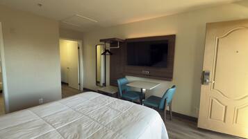 Una habitación de hotel con cama, escritorio, dos sillas, televisor y puerta.