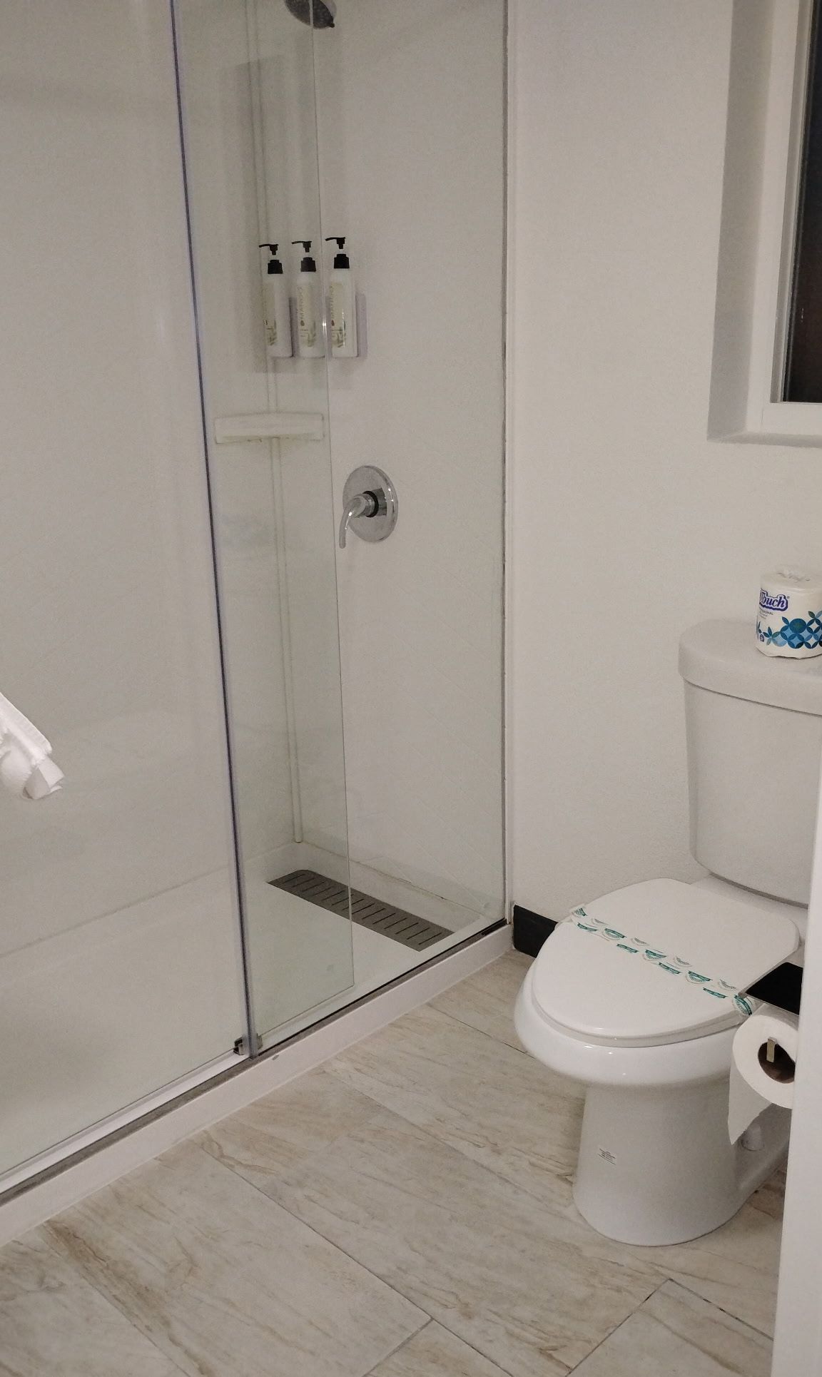 A modern bathroom with a glass-enclosed shower, a toilet with a paper towel holder, and a toilet paper roll.