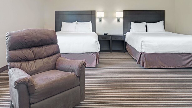 A hotel room with two beds, a large armchair, bedside tables, and a striped carpet.