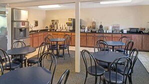 A hotel dining area with round tables and chairs, a kitchen in the background, and a sign indicating a coffee cooler.