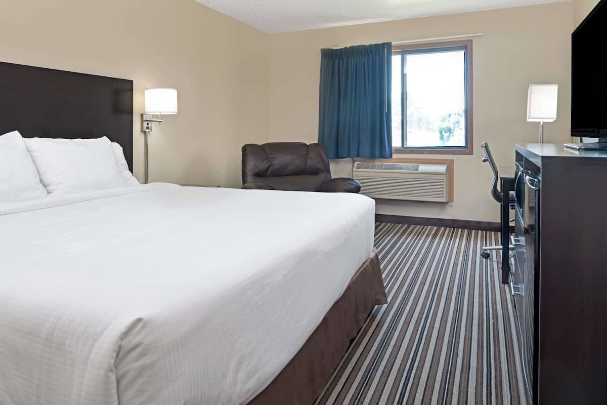 Habitación de hotel con una cama grande, un escritorio con silla, televisor y ventana con cortinas.