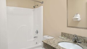 A bathroom with a white bathtub, a sink with a granite countertop, and a toilet.