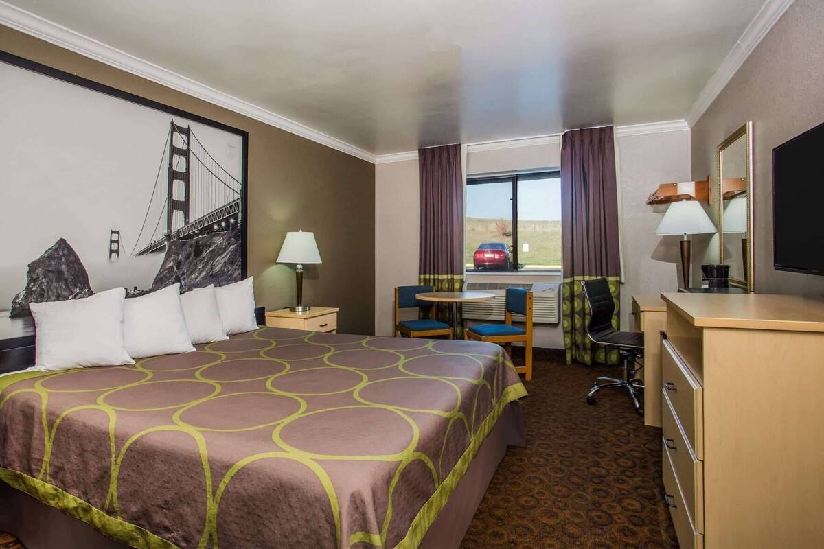 A hotel room with a large bed, a desk, a chair, a TV, and a window with curtains.