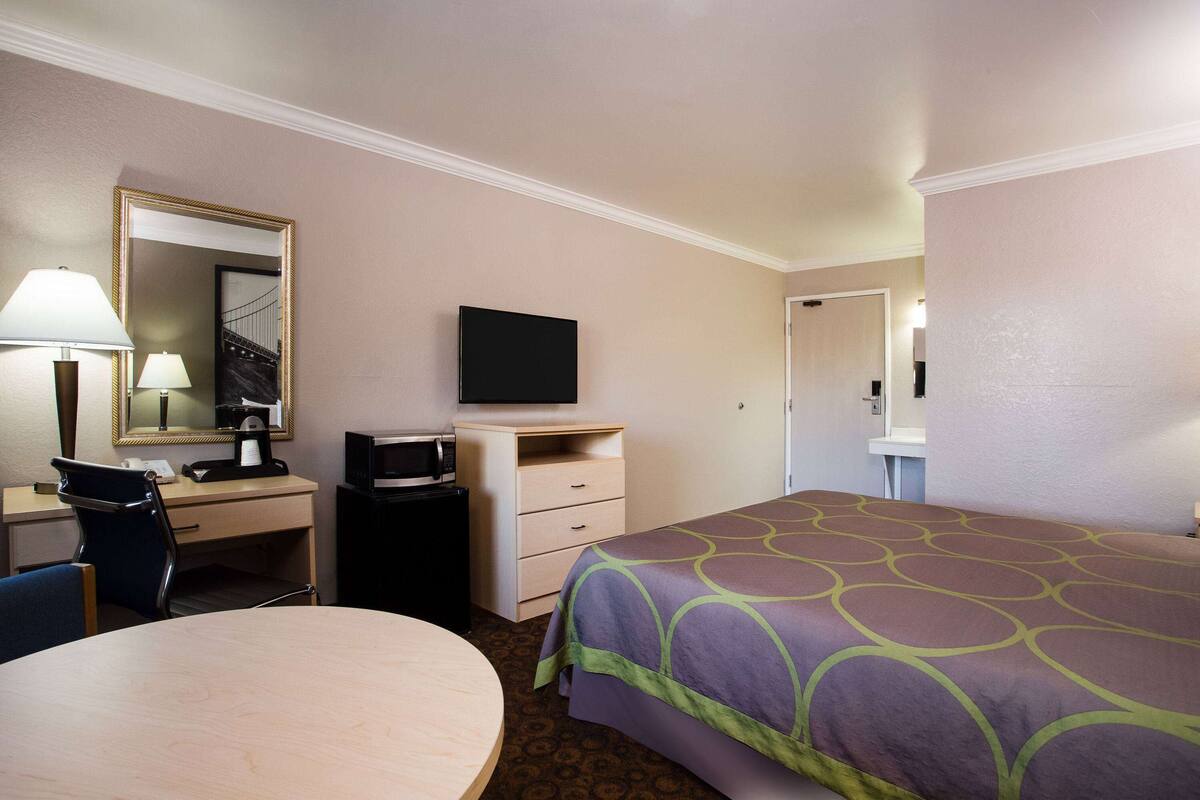 A hotel room with a bed, a desk with a chair, a television, a desk lamp, and a mirror.
