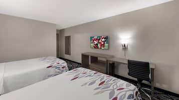 A hotel room with two beds, a desk, a chair, a TV, and a wall-mounted light.