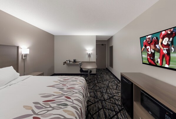 A hotel room with a bed, a desk, a chair, a television, and a microwave.