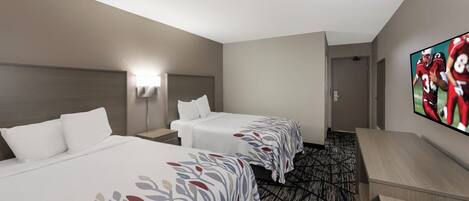 A hotel room with two beds, a TV on the wall, and a patterned carpet.