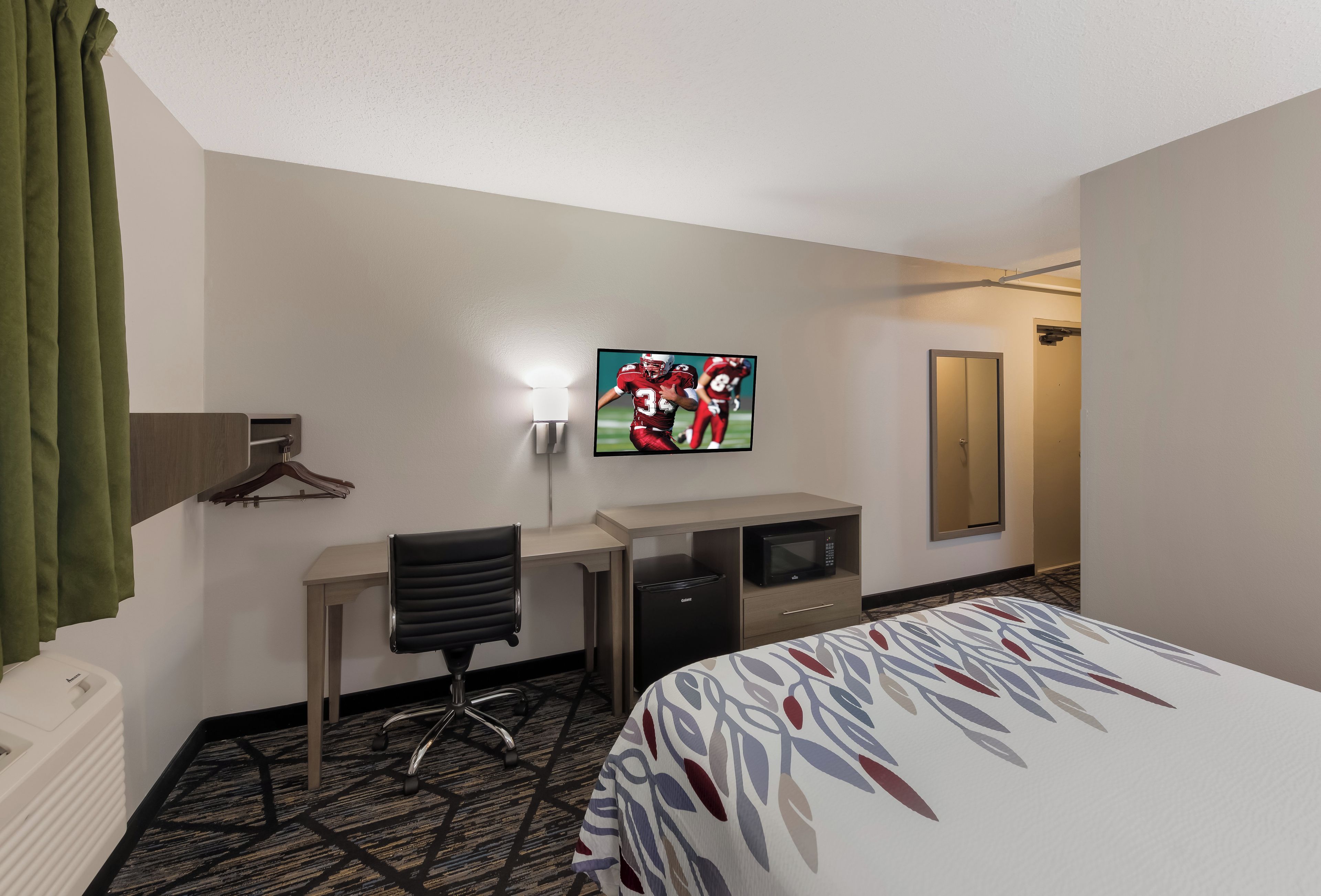 A hotel room with a bed, a desk, a chair, a television, a microwave, and a closet.