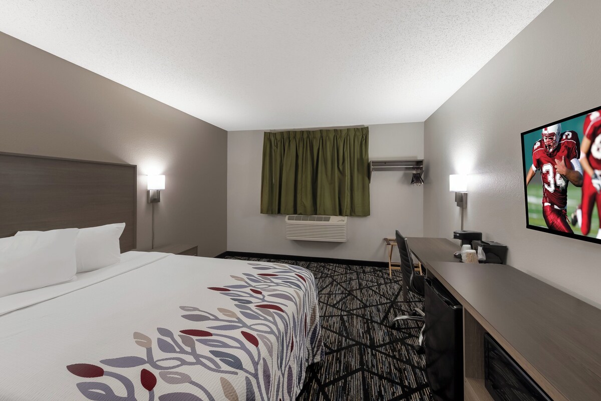 A hotel room with a bed, a desk, a TV, and an air conditioning unit.