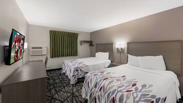 A hotel room with two beds, a flat-screen TV, an air conditioning unit, a green curtain, and a patterned carpet.