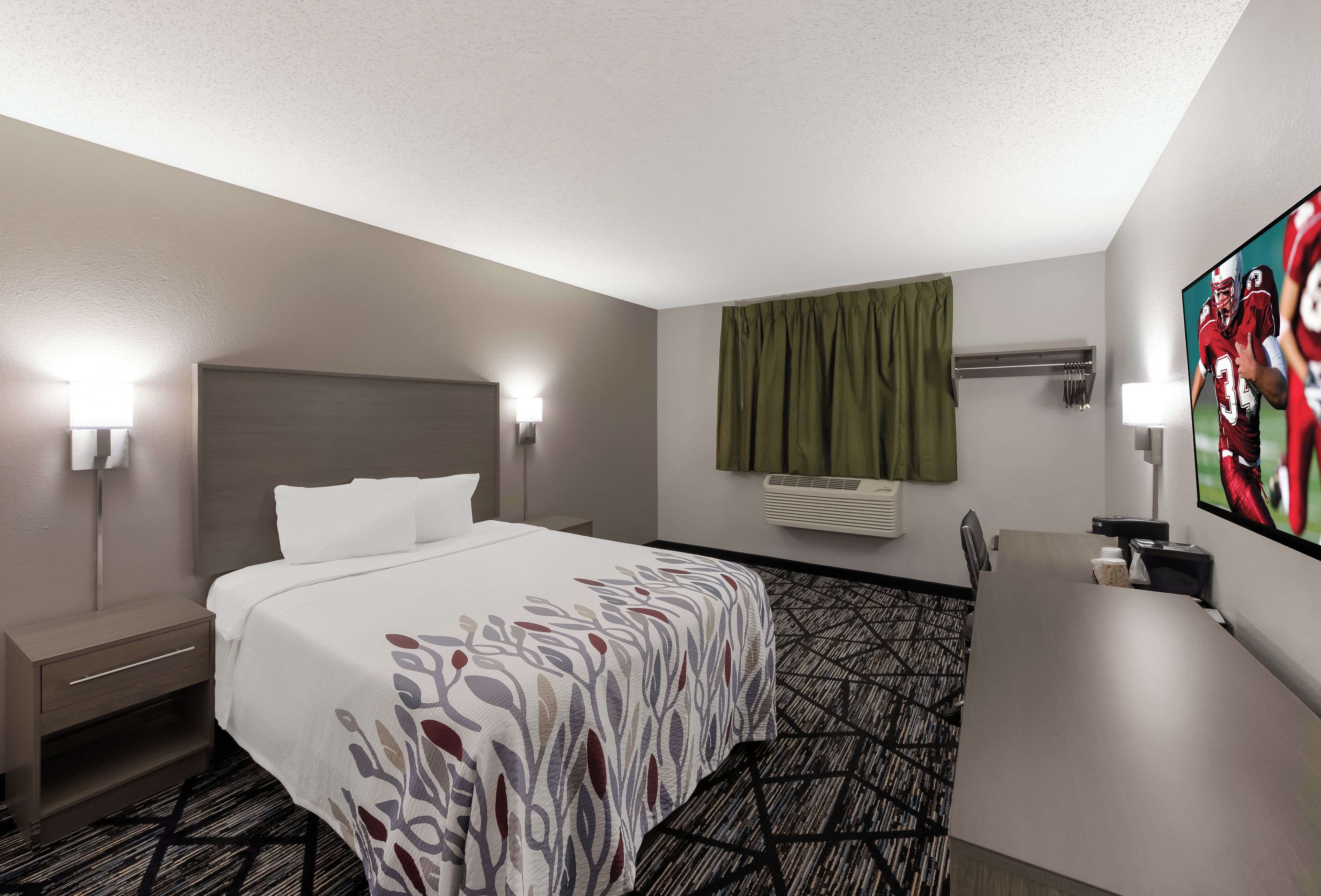Habitación de hotel con cama, mesitas de noche, escritorio, silla, televisor y ventana con cortinas.