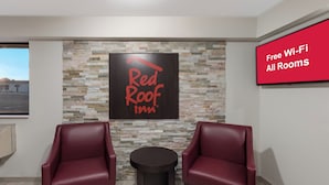 A Red Roof Inn room with a stone wall, two red leather chairs, a small table, and a sign stating "Free Wi-Fi All Rooms". - Red Roof Inn Mansfield (Mansfield)