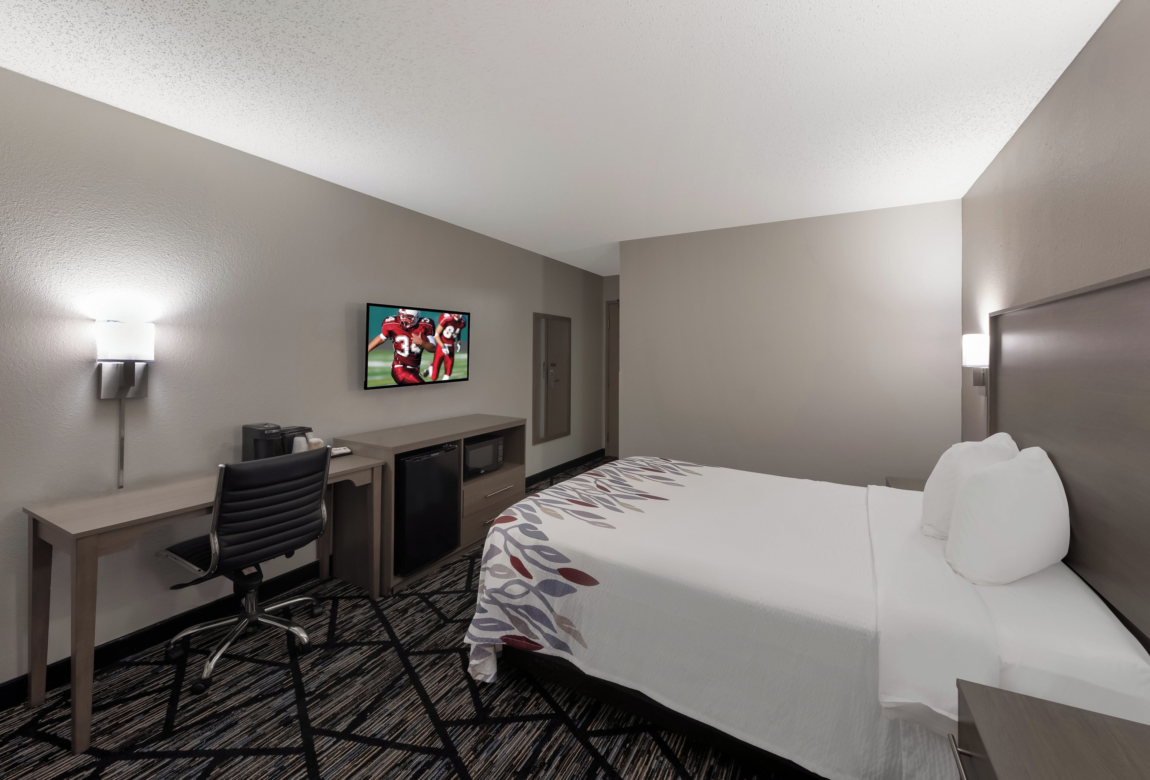 A hotel room with a bed, a desk, a chair, a television, and a microwave.