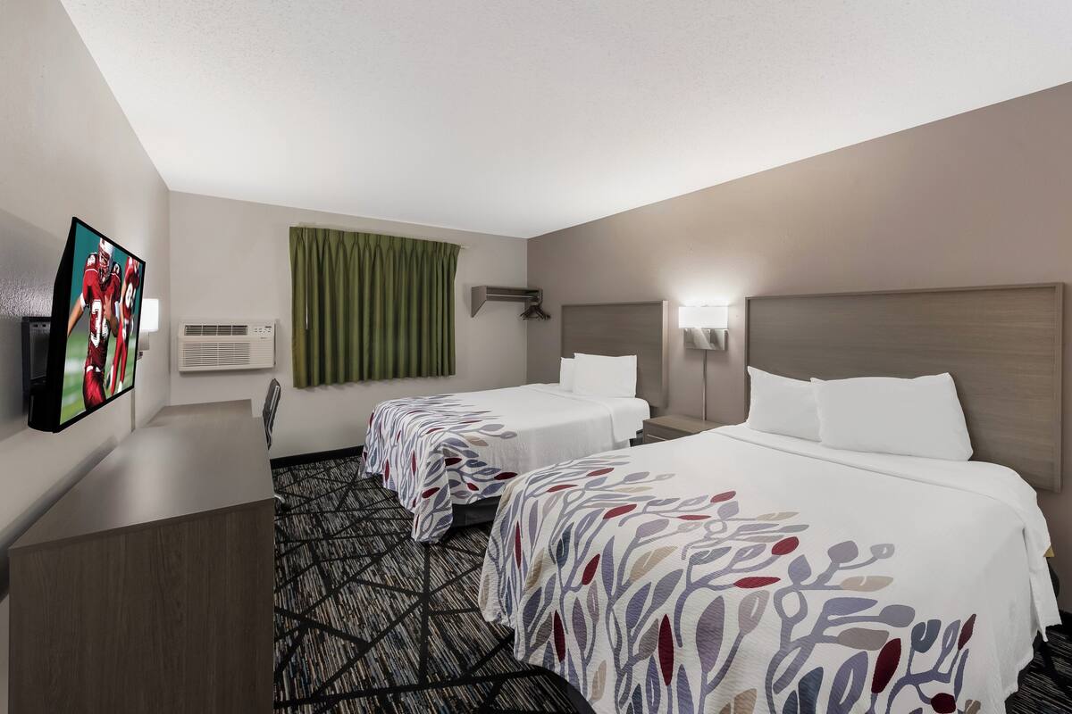 A hotel room with two beds, a TV, an air conditioner, and a patterned carpet.