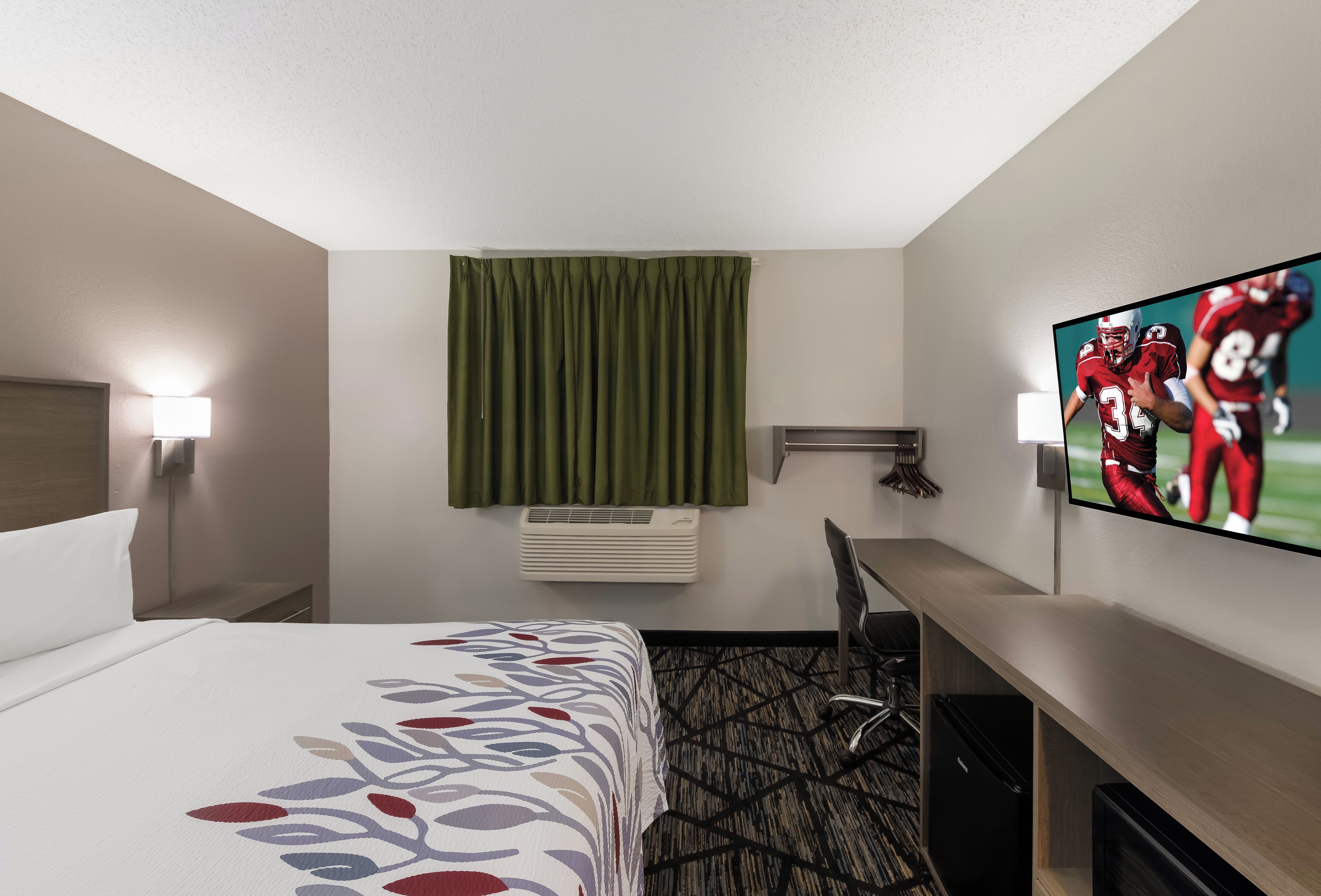 Habitación de hotel con cama, escritorio, silla, televisor y aire acondicionado.