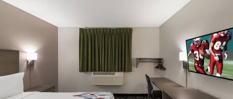 Habitación de hotel con cama, escritorio, silla, televisor y aire acondicionado.