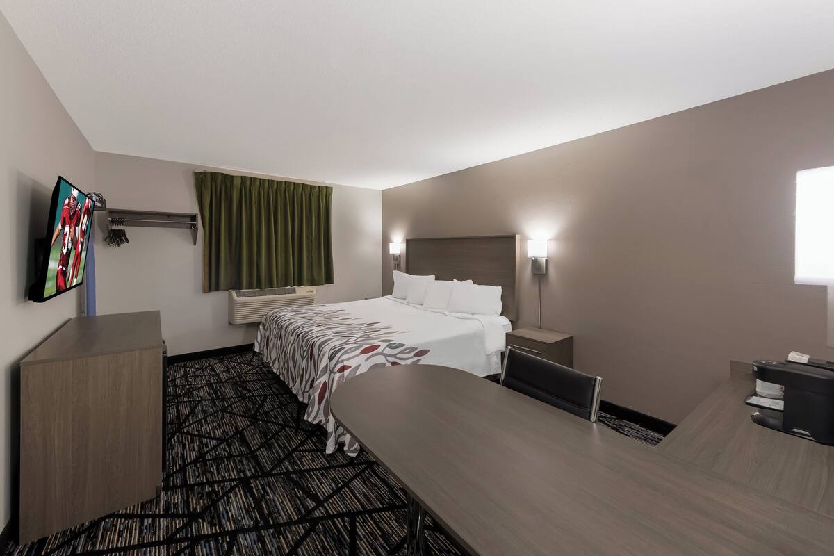 A hotel room with a bed, a desk, a flat-screen TV, a desk lamp, and a coffee machine.