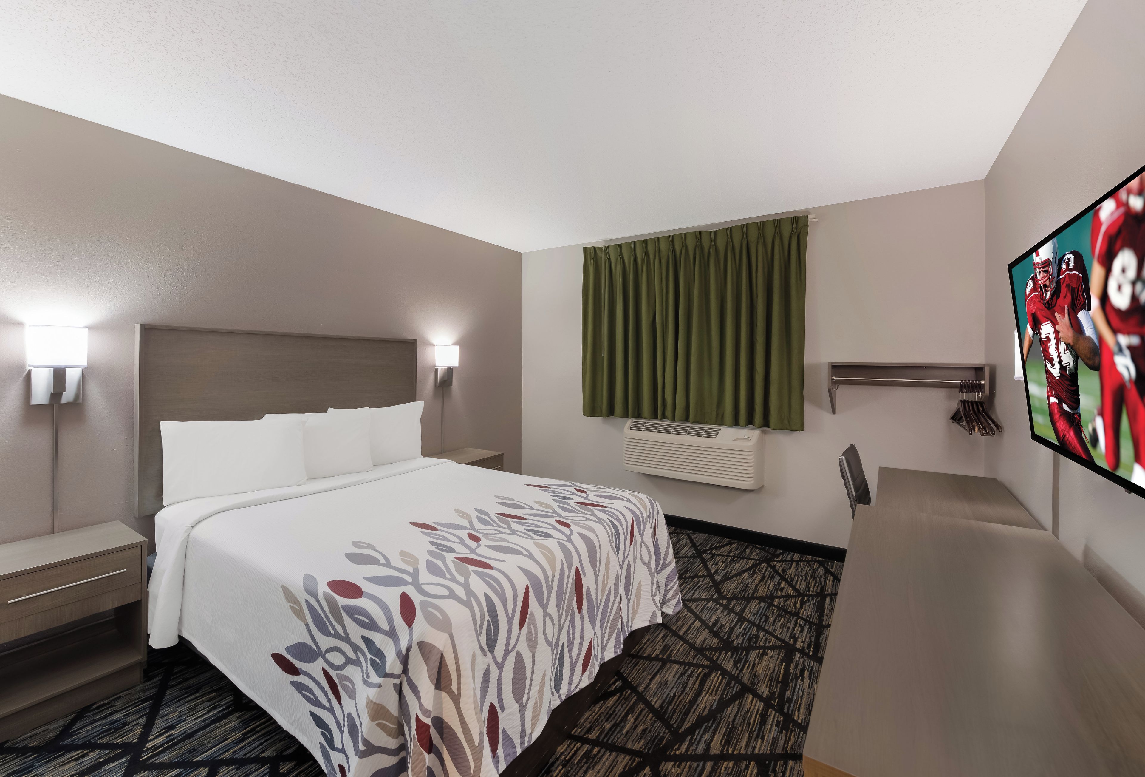 Ein Hotelzimmer mit einem Bett, Nachttischlampen, einem Flachbildfernseher, einem Fenster mit Vorhängen und einer Klimaanlage.