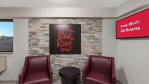 Habitación de Red Roof Inn con pared de piedra, dos sillones de cuero, una mesita y un cartel que indica acceso a Wi-Fi gratuito en todas las habitaciones.