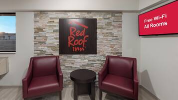 A Red Roof Inn room with a stone wall, two leather chairs, a small table, and a sign indicating free Wi-Fi in all rooms.