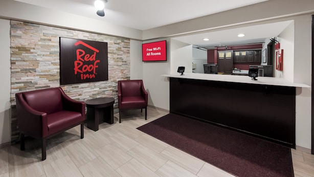 A Red Roof Inn reception area with a stone wall, two leather chairs, a small table, and a counter with a Dell computer. - Red Roof Inn Mansfield (Mansfield)