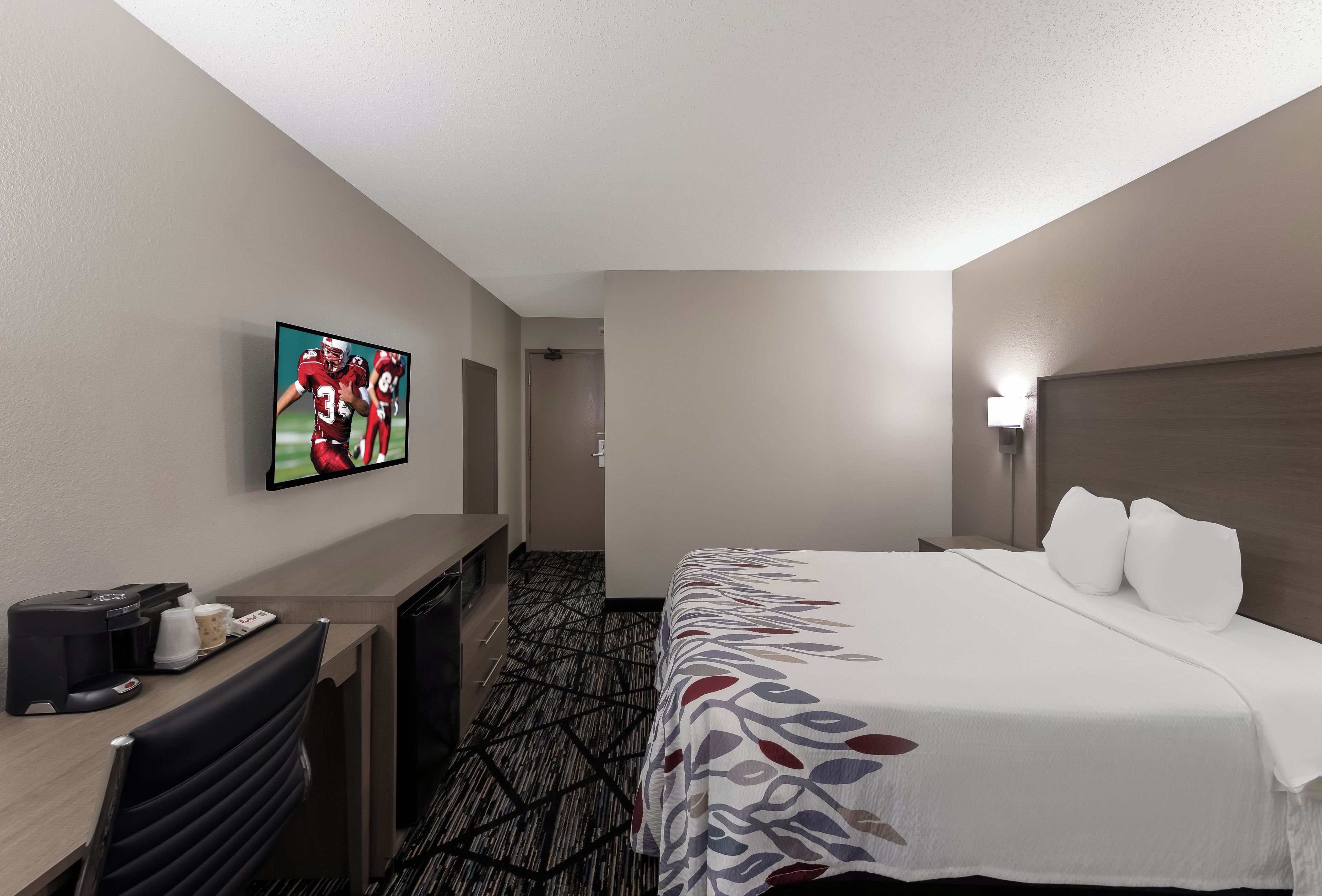 A hotel room with a bed, a desk, a television, and a coffee machine.