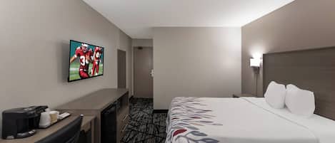 Quarto de hotel com cama, escrivaninha, televisão e máquina de café.