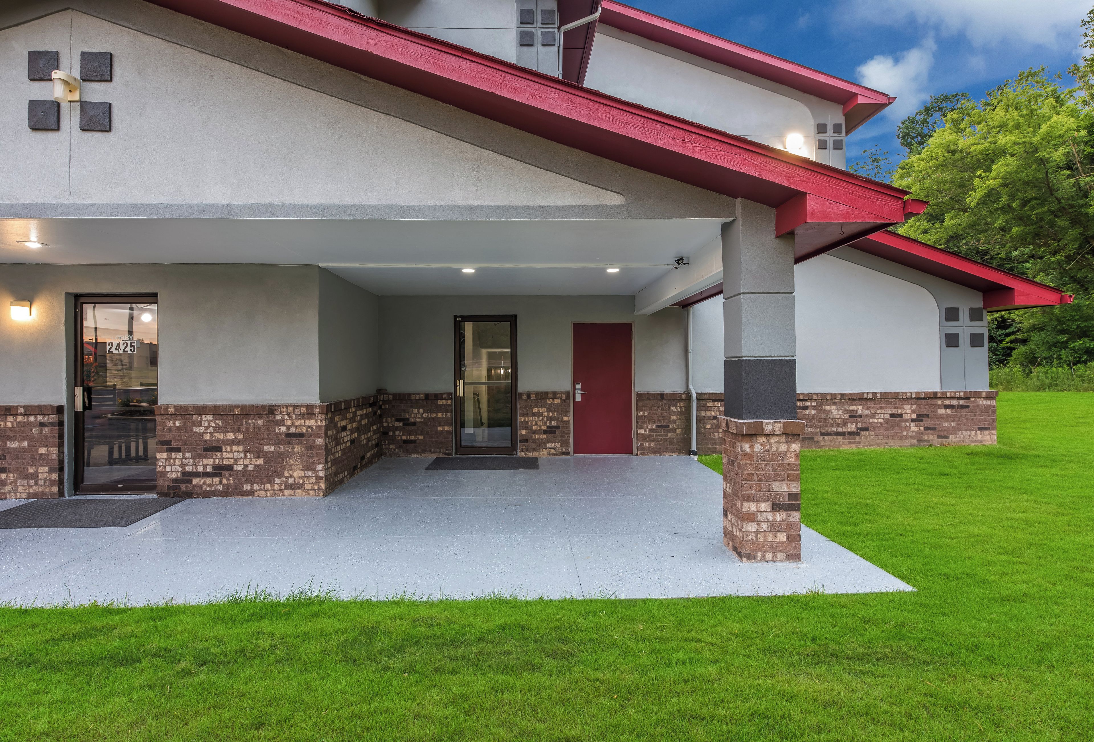 A two-story house with a covered porch, a red door, and a brick base.