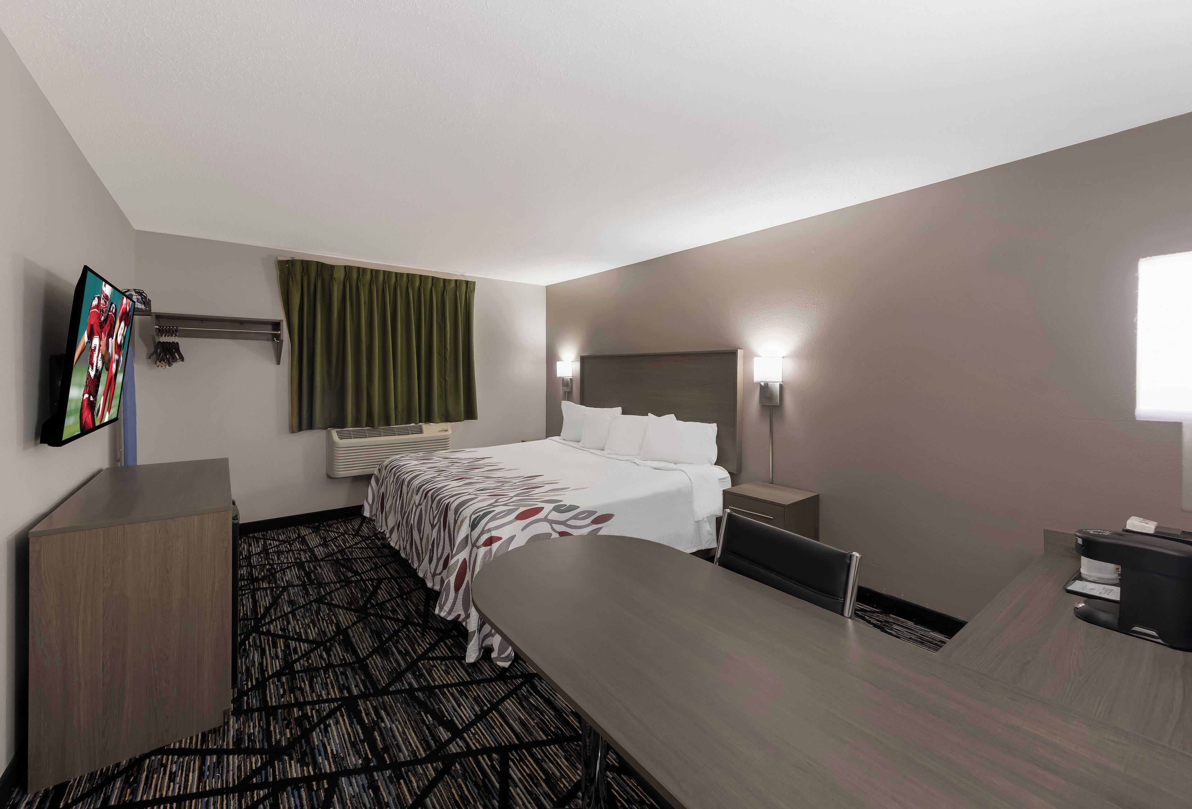 A hotel room with a bed, bedside tables, a desk, a chair, a television, and a window with curtains.